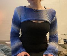 a woman sitting on top of a bed wearing a black shirt and blue knitted sweater