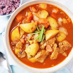 a bowl of stew with meat, potatoes and carrots next to a plate of rice