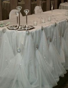 a table topped with lots of glasses next to a white table cloth covered tablecloth