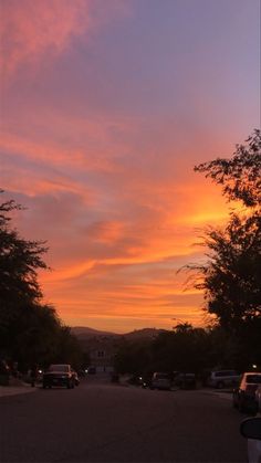 the sun is setting over some trees and cars