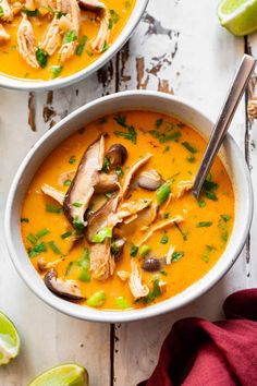 two bowls of soup with chicken, mushrooms and cilantro on the side next to limes