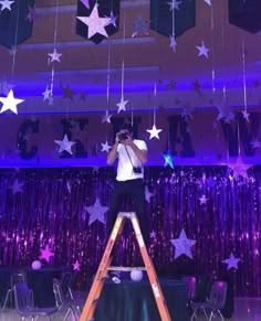 a man standing on a ladder in front of a stage with stars hanging from the ceiling