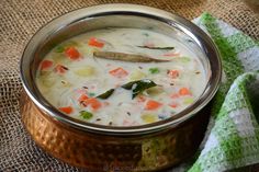 a metal bowl filled with soup on top of a green and white cloth next to a spoon