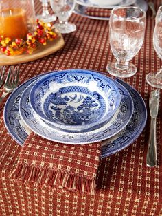 a blue and white plate sitting on top of a table next to wine glasses, silverware and candles