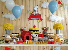 a table filled with lots of food and balloons on top of a wooden wall behind it