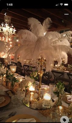 an image of a table setting with white feathers on it and candles in the center