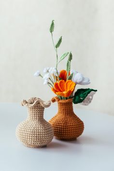 two crocheted vases with flowers in them sitting on a table next to each other