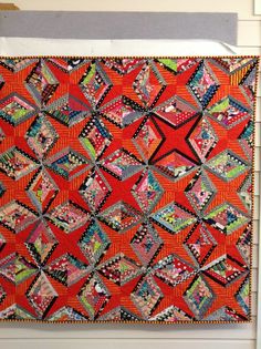 an orange quilt hanging on the wall in front of a white door with a black and red design