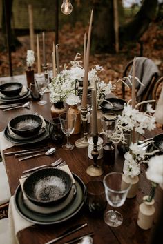 the table is set with black and white plates, silverware, flowers and candles