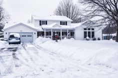 a car parked in front of a white house covered in snow next to some trees