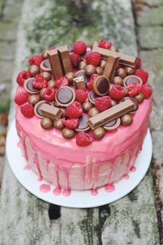 a pink cake with chocolate and raspberries on top sitting on a wooden table