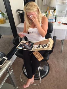 a woman sitting in a chair reading a book and holding her nose to her mouth