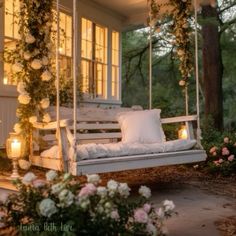 a white porch swing with pillows and flowers on the front lawn at night, lit by candles