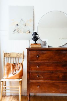 a wooden dresser sitting next to a mirror on top of a wall near a chair