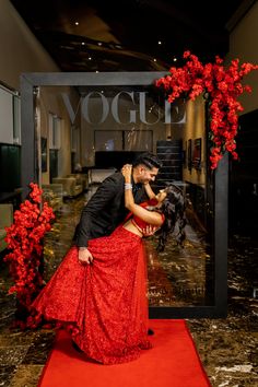 a man and woman are kissing in front of a red carpeted area with flowers