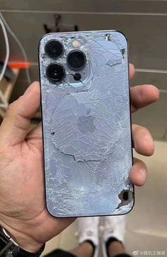 someone holding up their cell phone with the cracked glass on it's back side