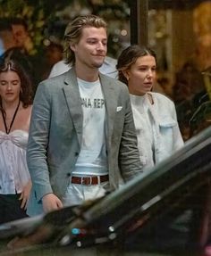 two people walking down the street in front of a car and one person is wearing a t - shirt