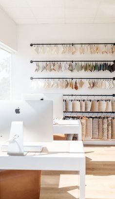 a white desk topped with a laptop computer next to a wall filled with hanging items