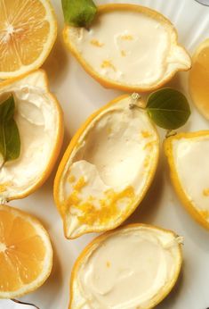 some oranges are cut in half and sitting on a white plate with green leaves