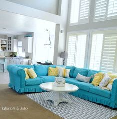 a living room with blue couches and yellow pillows on the rug in front of windows