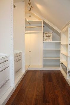 an empty walk in closet with white shelving and wood flooring on the side