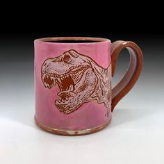 a pink and brown mug with an image of a t - rex on the side