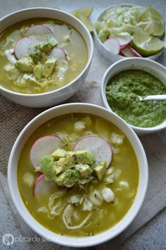 three bowls filled with soup and vegetables on top of a cloth covered table next to lime wedges