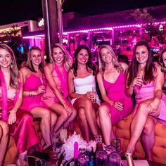 a group of women sitting next to each other in pink dresses on a couch at a party