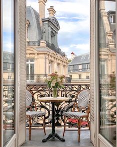 an open balcony with two chairs and a table in front of the window looking out at buildings