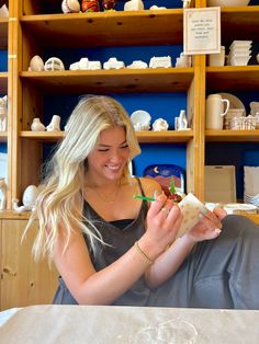 a woman sitting at a table with a sandwich in her hand