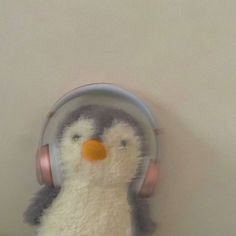 a small stuffed penguin with headphones on its face is sitting in front of a white wall