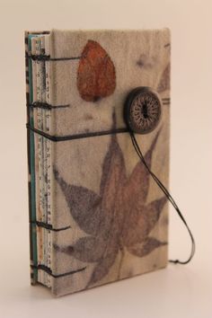 a small book with a button on the front cover and an image of leaves painted on it