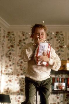 a young boy standing on top of a chair holding a box and blowing bubbles in the air