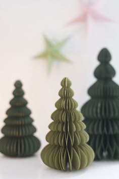 three green paper christmas trees sitting next to each other on a white counter top with a star in the background