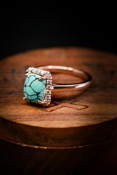 a turquoise stone and diamond ring sitting on top of a wooden table next to a piece of wood