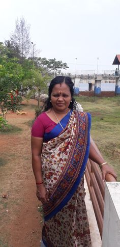 a woman in a sari standing on a wooden bench next to a river and bridge