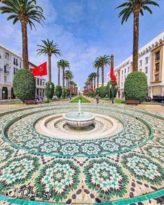 a fountain surrounded by palm trees in the middle of a street with buildings and flags