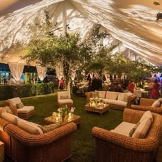 an outdoor event with wicker furniture and white draping on the roof, surrounded by greenery