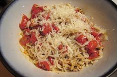 a white bowl filled with pasta covered in cheese and tomato sauce on top of a wooden table