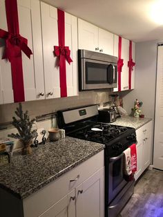 a kitchen decorated for christmas with white cabinets and black stove top oven, silver counter tops and red bows on the wall