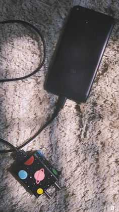 a cell phone hooked up to a charger on a carpeted floor with an ipod plugged into it