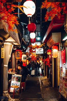 an alley way with lanterns hanging from the ceiling and people walking down it at night