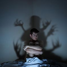 a man sitting in bed with his arms crossed and shadow cast on the wall behind him