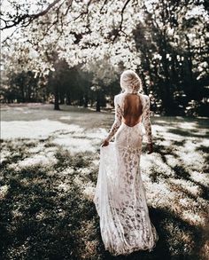 a woman in a white dress is walking through the grass with her back to the camera