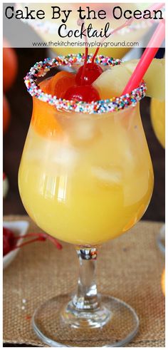 a yellow cocktail with a cherry garnish on the rim and topped with sprinkles