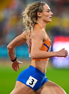 a woman running on a track in an orange top and blue shorts