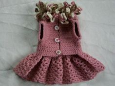 a pink crocheted dress with flowers on the collar and bottom, sitting on a white sheet