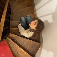 a woman sitting on the bottom of a wooden staircase