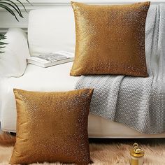 two pillows sitting on top of a white couch next to a blanket and pillow case