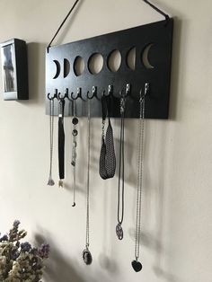 a black metal wall mounted jewelry holder with multiple necklaces hanging from it's sides